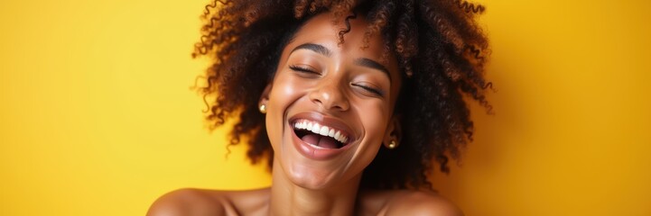 A joyful young woman with curly hair smiles brightly against a vibrant yellow backdrop, exuding happiness and confidence.