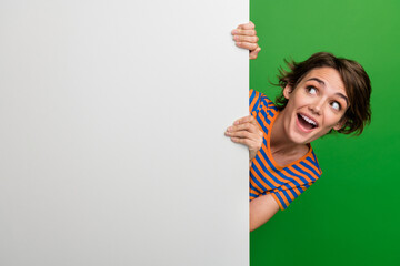 Canvas Print - Photo portrait of pretty young girl hide behind look white wall dressed stylish striped outfit isolated on green color background