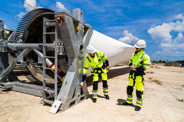 two engineers in safety gear inspecting a wind turbine blade section on a construction site. they ex