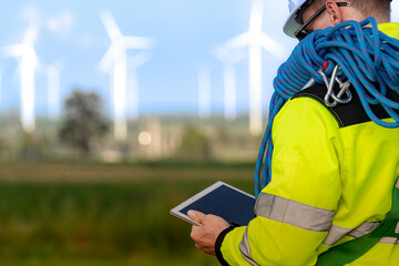 two engineers in high visibility jackets and helmets are inspecting a wind farm. one is holding a mo