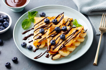 Wall Mural - Crepes, thin pancakes with chocolate sauce and fresh blueberries. Grey background. Closeup.