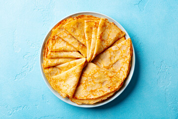Wall Mural - Crepes, thin pancakes on a plate. Blue background. Close up. Top view.