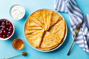 Wall Mural - Crepes, thin pancakes on a plate with honey, cherry jam and cream. Blue background. Top view.