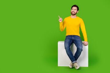 Poster - Full length photo of handsome young guy point look empty space sit cube dressed stylish yellow garment isolated on green color background