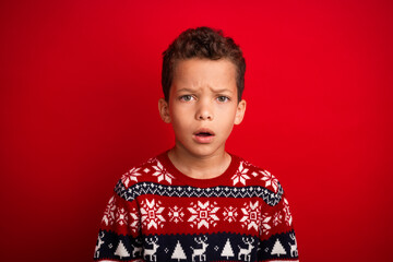 Sticker - Photo portrait of charming small boy scared shocked look celebrate christmas dressed knitted sweater isolated on red color background