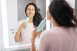 © Home-stock - Happy woman looking at mirror and brushing teeth with water floss, doing everyday morning routine in bathroom. Lady using portable irrigation system