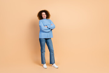 Canvas Print - Full body photo of young confident beautiful curly haired lady in blue knitted sweater folded hands isolated on beige color background