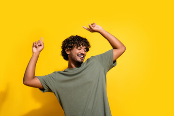 Canvas Print - Photo of carefree good mood guy with wavy hairstyle dressed khaki t-shirt dancing raising fingers up isolated on yellow color background