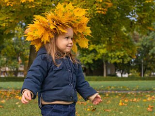 Little girl with a wreath of autumn maple leaves in the park wearing warm jacket