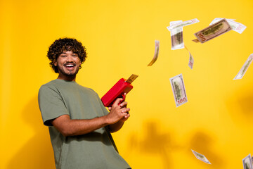 Canvas Print - Photo of overjoyed guy with wavy hair dressed khaki t-shirt throwing fluttering dollars with gun isolated on yellow color background