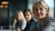 © Maria Mikhaylichenko - Confident mature businesswoman smiling during meeting with colleagues, showcasing leadership and positive workplace atmosphere in modern office setting.