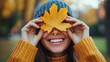 © Nijat - In an autumn park, a lovely, content woman covers her eyes with a yellow maple leaf.
