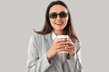 Poster - Young woman in stylish suit with cup of coffee on light background, closeup