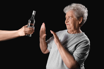 Wall Mural - Senior woman rejecting bottle of vodka on black background