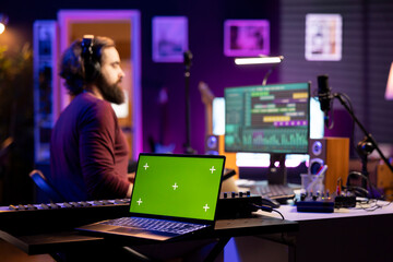 Leinwandbilder - Audio engineer adding sound effects on tunes by using daw software interface, editing music next to greenscreen display on laptop. Young artist working on post production in home studio.