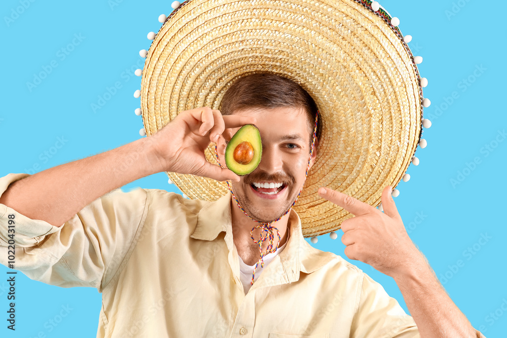 Young Mexican man in sombrero and with avocado on blue background