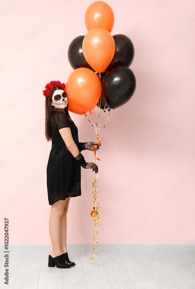 Young woman dressed for Halloween with balloons near light wall