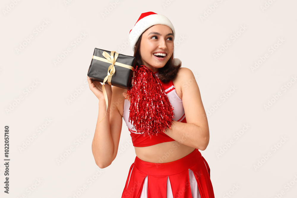 Beautiful cheerleader in Santa hat with pompom and gift box on white background