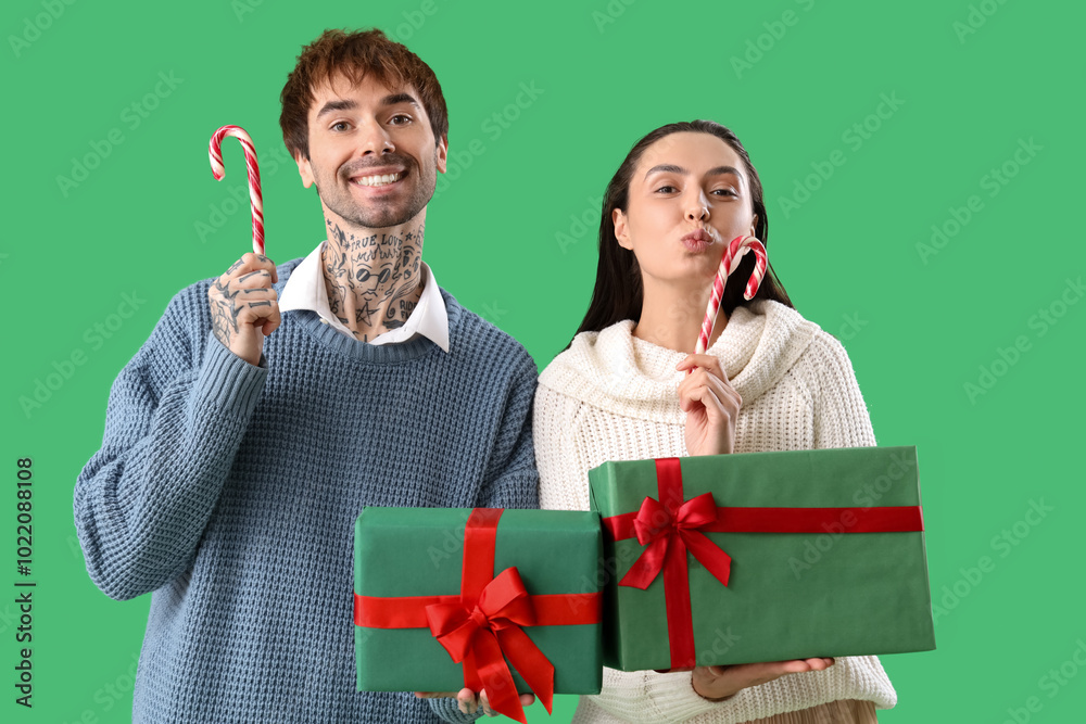 Young couple with Christmas presents and candy canes on green background