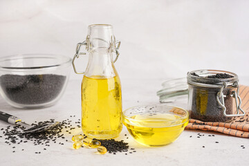 Bottle and bowl of oil with sesame seeds on white background