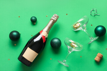 Bottle of champagne with glasses, Christmas balls, cork and confetti on green background