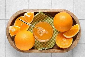 Wooden tray with glass of tasty juice and fresh oranges on white tile background