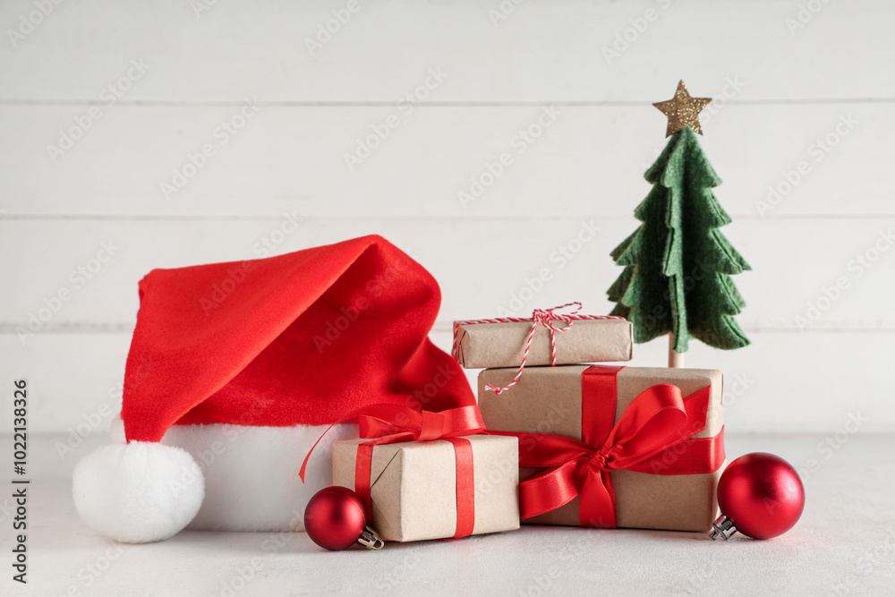 Santa hat with Christmas gift boxes, balls and decorative fir tree on white table