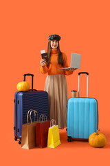 Wall Mural - Female tourist in autumn clothes with laptop and bags on orange background