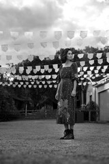 Black and white photograph of young woman in dress in small old town square with flags