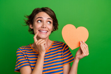 Poster - Portrait of gorgeous minded person finger touch chin hold heart card look empty space isolated on green color background