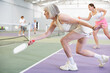 © JackF - Portrait of positive fit elderly woman playing pickleball on indoor court, swinging paddle to return ball over net ..