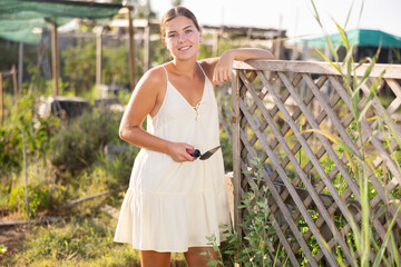 Young woman in dress posing near fence in garden