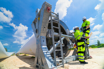 two engineers in safety gear inspecting a wind turbine blade section on a construction site. they ex