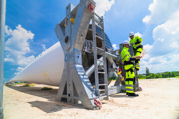 two engineers in safety gear inspecting a wind turbine blade section on a construction site. they ex