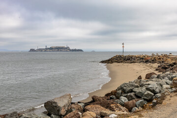 View of Alcatraz Island from Crissy Field, San Francisco, California, showcasing the historic prison shrouded in a tranquil, cloudy seascape.