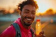 © btiger - Latino male athlete holding water bottle on track at sunset laughing in sportswear