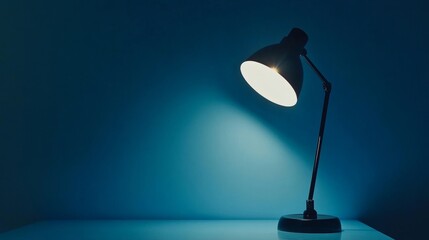 A black desk lamp shining directly on a blue wall, creating a focused, minimalist lighting effect with soft, calming tones.