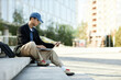 © Seventyfour - Side view of Asian male IT programmer writing code on laptop looking at computer screen while sitting on concrete steps in city street, copy space