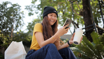 gen z eco go green woman asia sit happy relax at tree public park city life enjoy typing mobile phon
