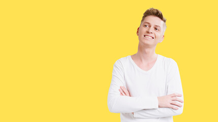 Man with a white shirt and arms crossed is smiling. He is looking to the right. The background is yellow