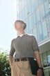 © Seventyfour - Vertical shot of Asian businessman in minimalist classy outfit wearing gray polo standing in sunlight outside office building in city street, copy space