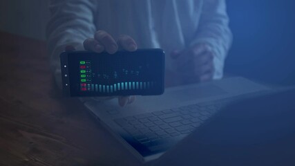 Poster - A man behind a laptop with a smartphone in his hand demonstrates his screen in the dark on which there is footage with a graph and digital indicators that are moving. Financial success concept. Cg