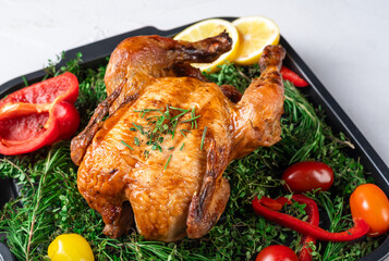 A golden roasted chicken seasoned with herbs on a tray, surrounded by fresh sprigs of rosemary, thyme, lemon slices, red and yellow bell peppers, and cherry tomatoes. Perfect for food blogs