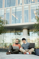 Poster - vertical shot of diverse team of two male it programmers working on laptops collaboratively sitting 
