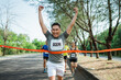 © Odua Images - asian male runner crossing finish line celebrating victory with hands up gesture