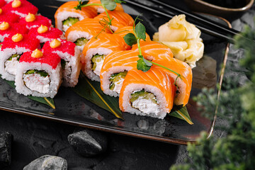 Delicious sushi rolls set served on black plate being presented on dark background