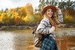 © maxbelchenko - Female traveler with a backpack and a hat enjoying autumn hiking along the river. Active lifestyle. Hiking