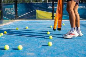 Many yellow tennis balls on blue court. Preparing for game. Athlete's foot in sneakers. Popular active new game padel. Side view.