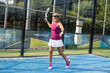 © vera - Woman in red t-shirt and white sport skirt stay on court hold rackets and play panel tennis. blue court. popular active new game padel.