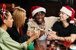© LIGHTFIELD STUDIOS - Young professionals toast with drinks, sharing laughter and holiday spirit at a corporate party.